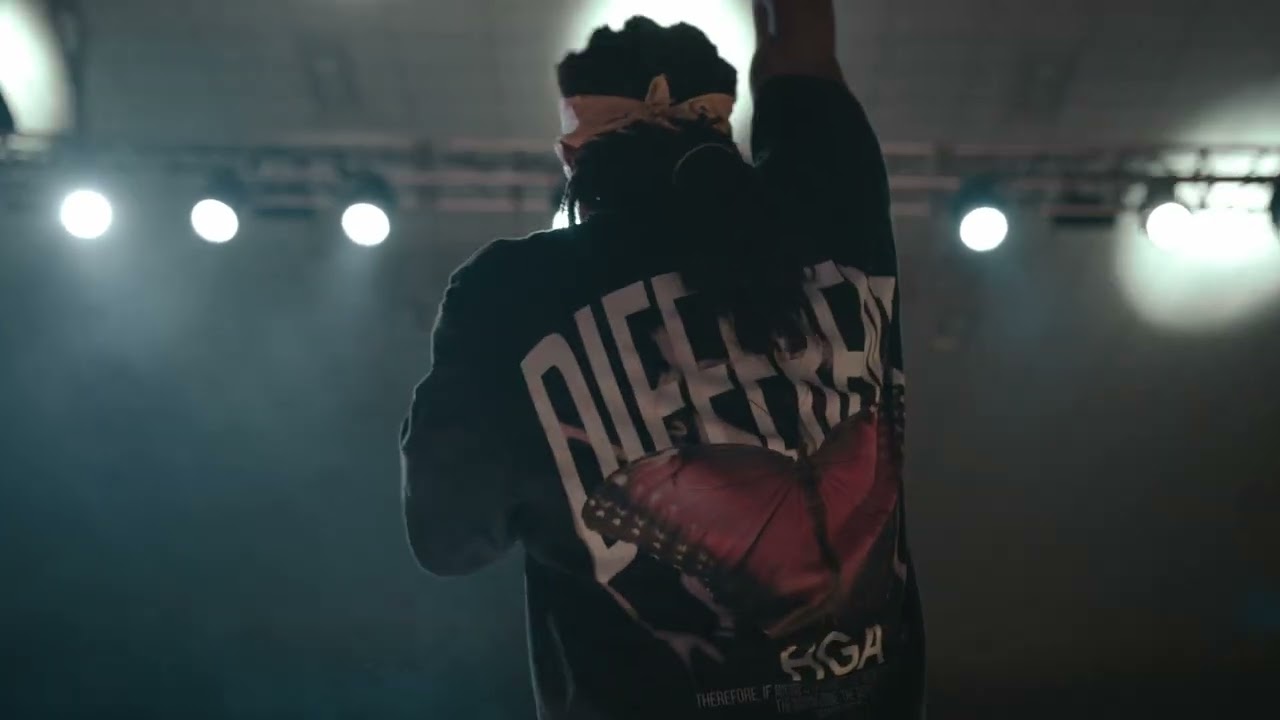 A performer on stage under bright lights, a still from a Dammon Creative music video